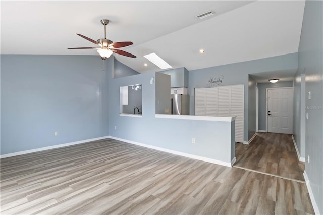 unfurnished room featuring visible vents, wood finished floors, vaulted ceiling with skylight, baseboards, and ceiling fan