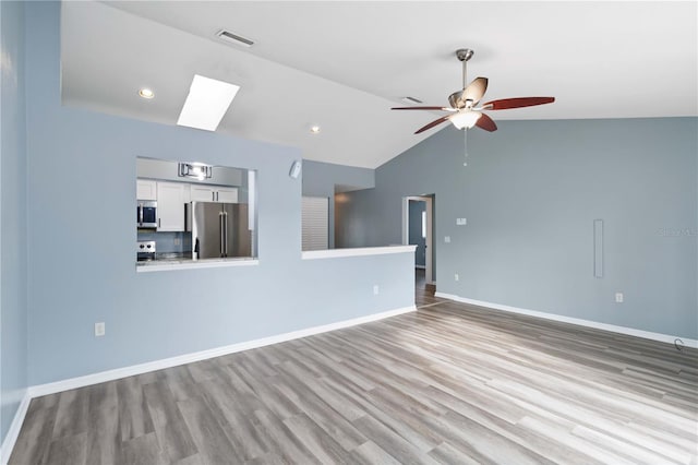 unfurnished living room with wood finished floors, baseboards, visible vents, ceiling fan, and lofted ceiling with skylight