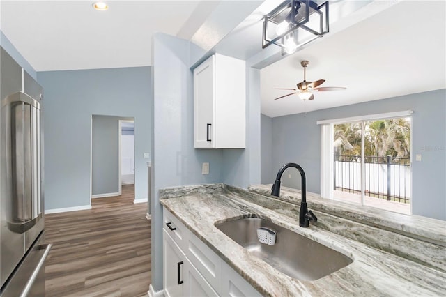 kitchen featuring a sink, light stone counters, white cabinetry, and stainless steel refrigerator