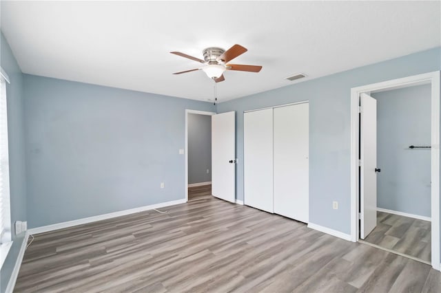 unfurnished bedroom featuring visible vents, wood finished floors, a closet, and baseboards