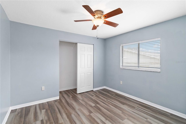 unfurnished bedroom featuring wood finished floors, baseboards, a closet, and ceiling fan