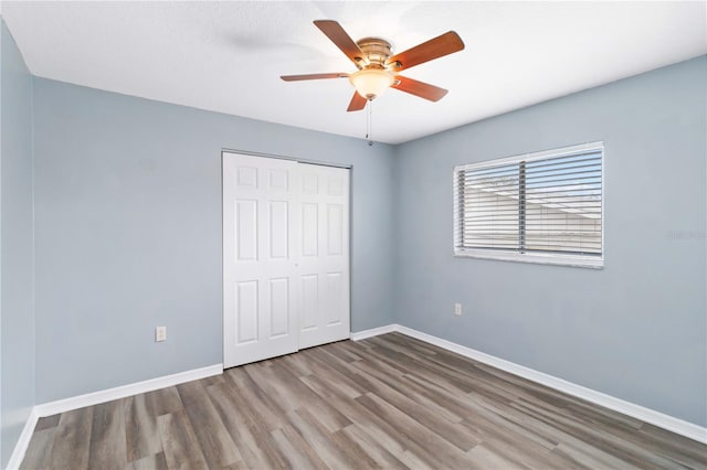 unfurnished bedroom featuring a closet, ceiling fan, baseboards, and wood finished floors