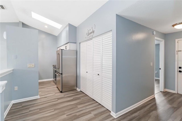 kitchen with light wood-type flooring, vaulted ceiling with skylight, baseboards, and freestanding refrigerator