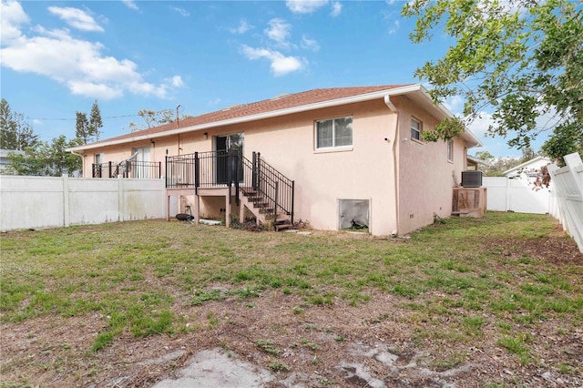 back of property featuring stairway, central AC, stucco siding, a lawn, and a fenced backyard