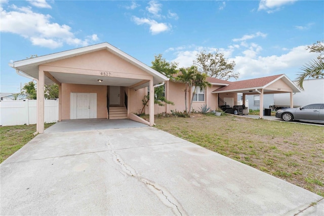 ranch-style house with a front lawn, fence, concrete driveway, stucco siding, and a carport