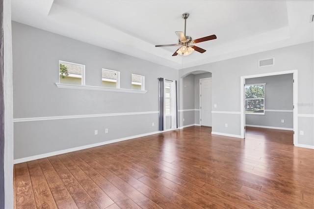 spare room featuring visible vents, a raised ceiling, arched walkways, and hardwood / wood-style flooring