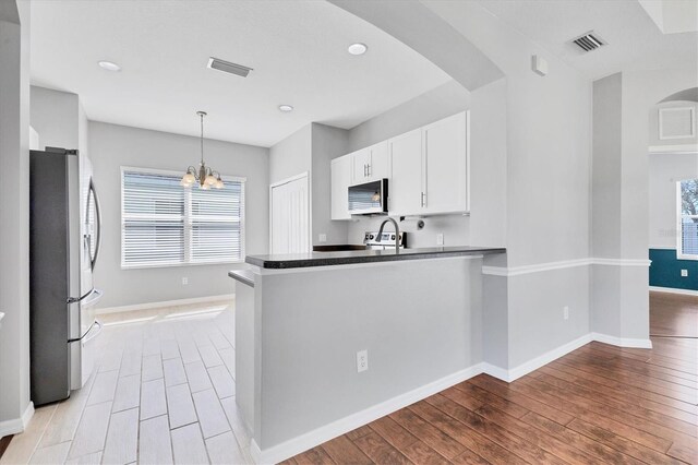 kitchen with visible vents, a peninsula, light wood-style floors, white cabinets, and stainless steel appliances