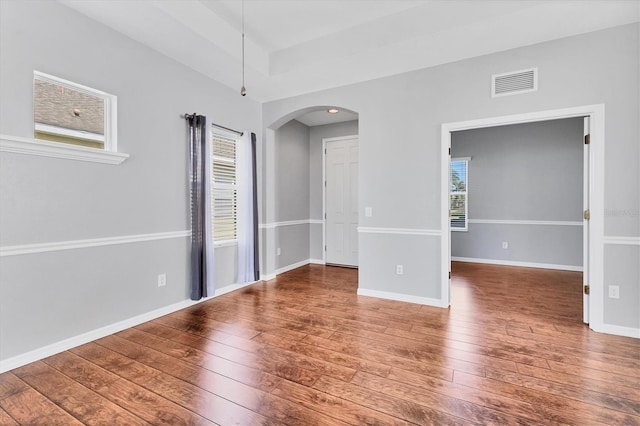 spare room featuring arched walkways, visible vents, wood-type flooring, and baseboards