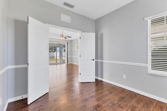 empty room with a ceiling fan, wood finished floors, visible vents, and baseboards