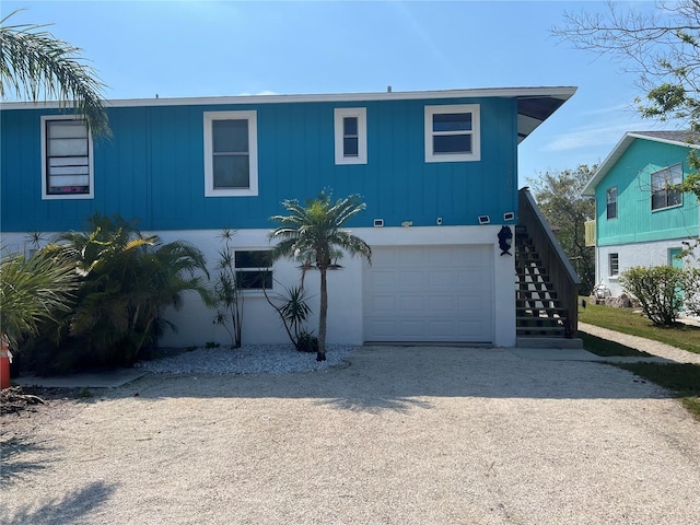 view of front of house featuring stairs, an attached garage, and gravel driveway