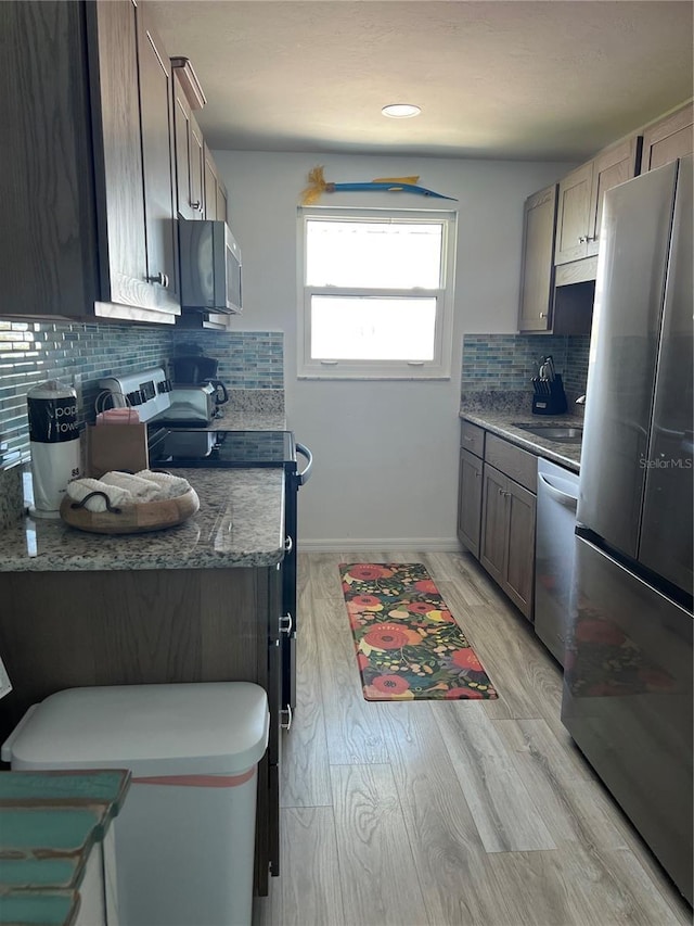 kitchen with a sink, tasteful backsplash, stainless steel appliances, light wood finished floors, and baseboards