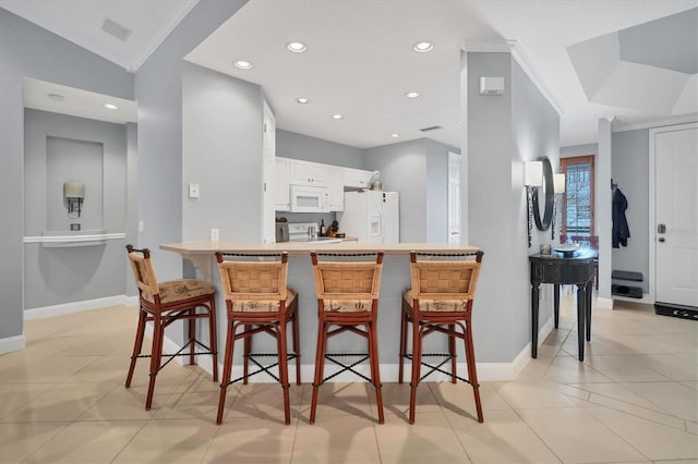 kitchen featuring crown molding, a kitchen breakfast bar, a peninsula, white cabinets, and white appliances