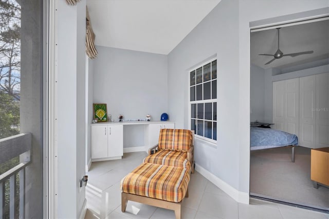 living area featuring light tile patterned flooring, a ceiling fan, and baseboards