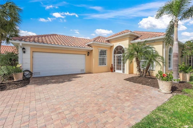 mediterranean / spanish-style house with a tiled roof, decorative driveway, an attached garage, and stucco siding