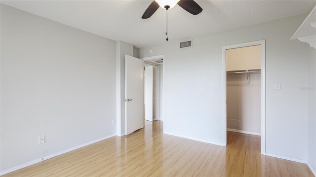 unfurnished bedroom featuring a walk in closet, wood finished floors, visible vents, and baseboards