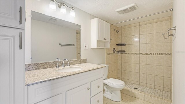 full bathroom featuring visible vents, toilet, a tile shower, tile patterned flooring, and vanity