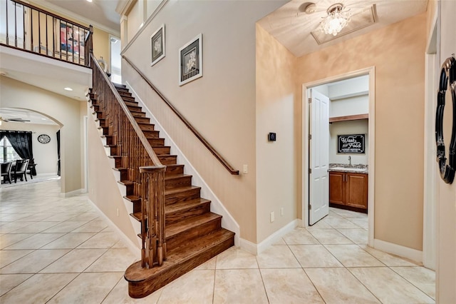 stairway featuring tile patterned floors, baseboards, arched walkways, and a high ceiling