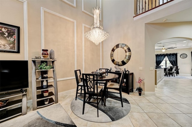 tiled dining room featuring arched walkways, ceiling fan with notable chandelier, a high ceiling, and baseboards