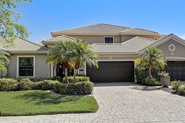 view of front of house with a front lawn, a tiled roof, stucco siding, decorative driveway, and a garage