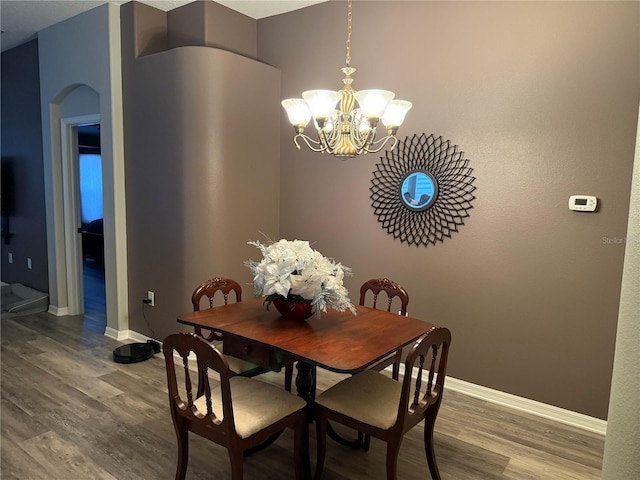 dining space with a chandelier, arched walkways, baseboards, and wood finished floors