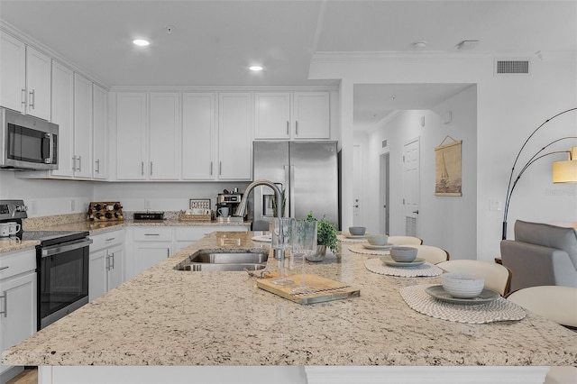 kitchen with visible vents, an island with sink, ornamental molding, stainless steel appliances, and a sink