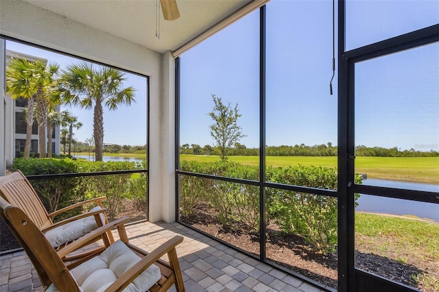 sunroom with ceiling fan and a water view