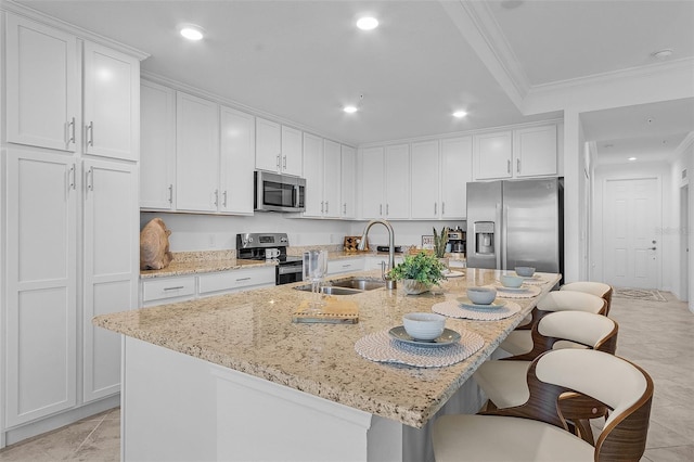 kitchen featuring a breakfast bar, ornamental molding, a sink, white cabinetry, and appliances with stainless steel finishes