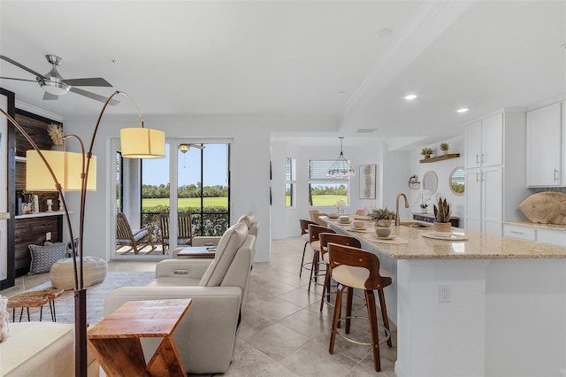 kitchen featuring a breakfast bar area, light stone counters, a sink, ornamental molding, and white cabinetry