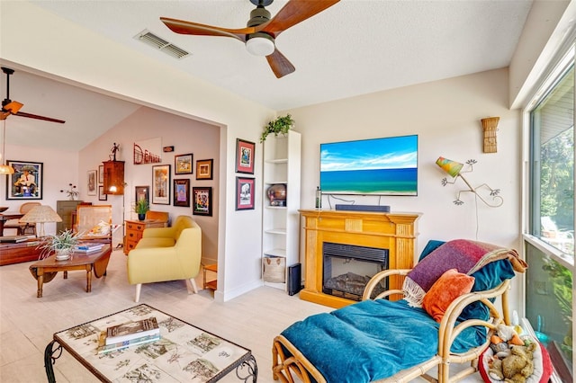 living room with visible vents, a fireplace, a textured ceiling, and a ceiling fan