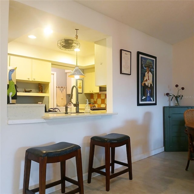 kitchen featuring light countertops, a kitchen bar, hanging light fixtures, white cabinets, and a raised ceiling