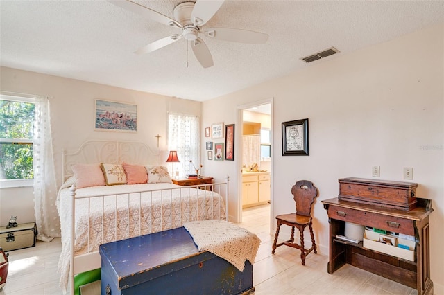 bedroom featuring visible vents, a textured ceiling, ensuite bathroom, and a ceiling fan