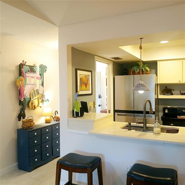 kitchen with freestanding refrigerator, a sink, light countertops, white cabinets, and a kitchen breakfast bar