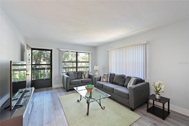 living room with a textured ceiling, light wood-type flooring, and baseboards