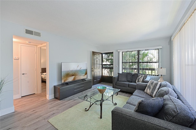 living room with light wood finished floors, visible vents, a textured ceiling, and baseboards