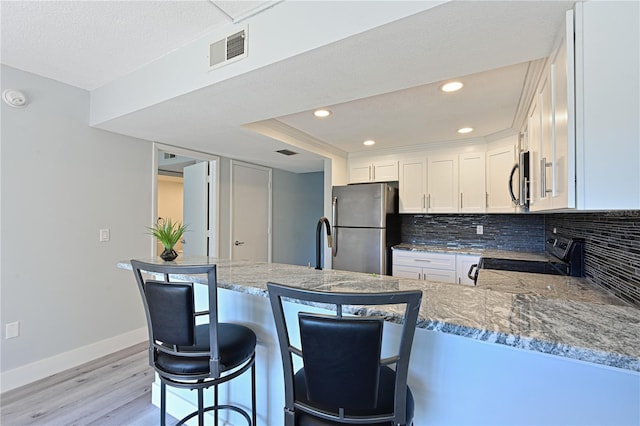 kitchen featuring visible vents, backsplash, stainless steel appliances, white cabinets, and light wood finished floors