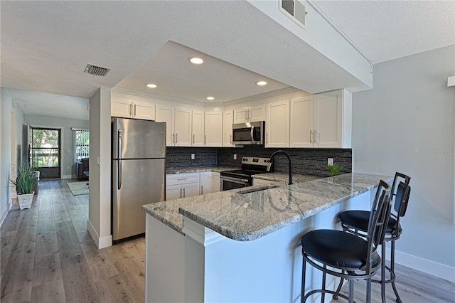 kitchen featuring visible vents, light wood-style flooring, stainless steel appliances, decorative backsplash, and light stone countertops