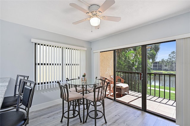 dining room with a water view, light wood-style flooring, a textured ceiling, baseboards, and ceiling fan