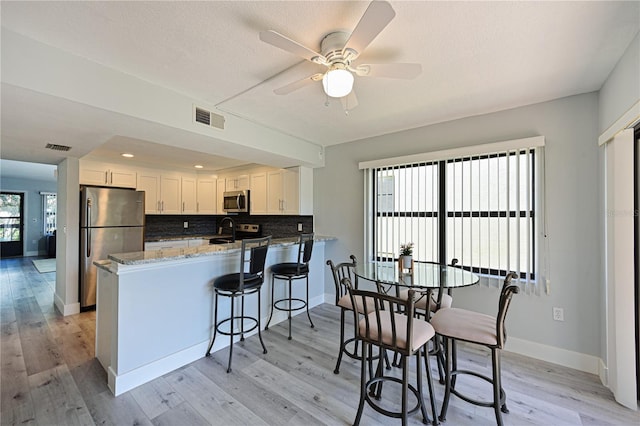 kitchen with visible vents, white cabinetry, appliances with stainless steel finishes, a peninsula, and light stone countertops