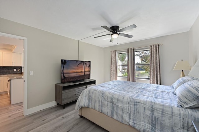 bedroom featuring light wood-style flooring, ceiling fan, baseboards, and a sink