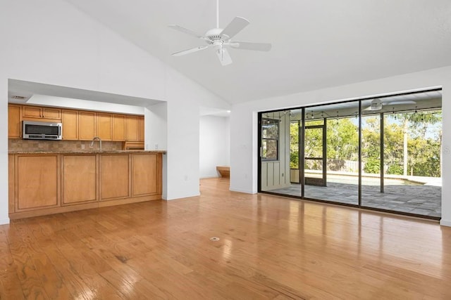 unfurnished living room featuring a sink, high vaulted ceiling, light wood-style flooring, and a ceiling fan