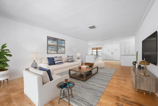 living area with visible vents, ornamental molding, and light wood finished floors