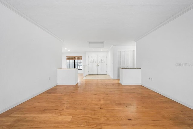 unfurnished living room featuring crown molding, light wood-style flooring, attic access, and baseboards