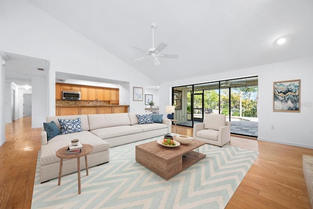 living area with ceiling fan, high vaulted ceiling, light wood-type flooring, and baseboards