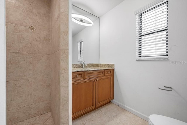 bathroom featuring tile patterned flooring, baseboards, toilet, a tile shower, and vanity