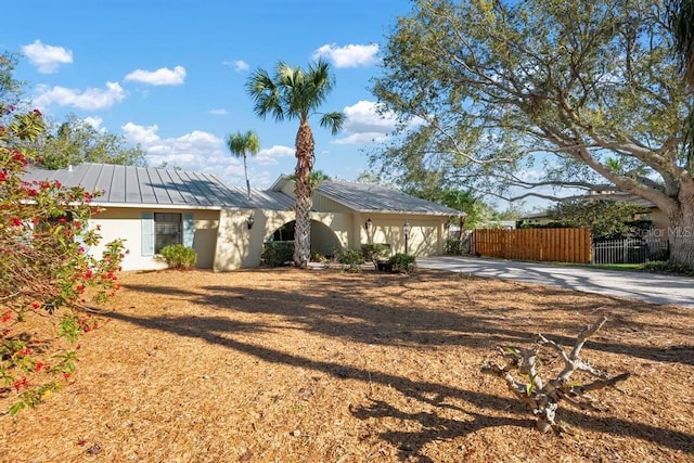 ranch-style home featuring fence, a standing seam roof, stucco siding, concrete driveway, and metal roof