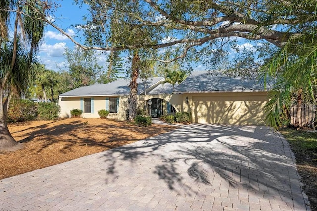 ranch-style house featuring a garage, decorative driveway, and stucco siding