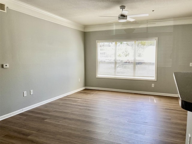 spare room featuring dark wood-type flooring, baseboards, ornamental molding, a textured ceiling, and a ceiling fan