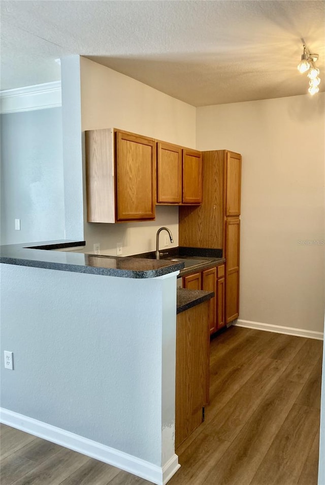 kitchen featuring dark wood finished floors, brown cabinets, dark countertops, and a sink