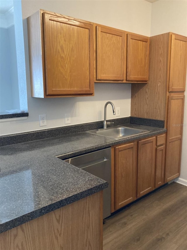 kitchen with dark wood-style floors, a sink, stainless steel dishwasher, dark countertops, and brown cabinets