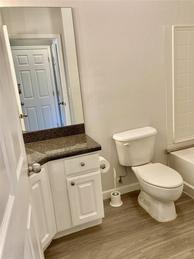 bathroom featuring vanity, wood finished floors, a bathing tub, baseboards, and toilet